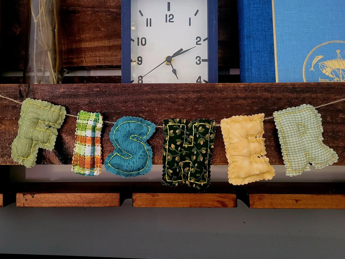 Handmade fabric letters spelling Fisher, sewn in mixed colors and patterns